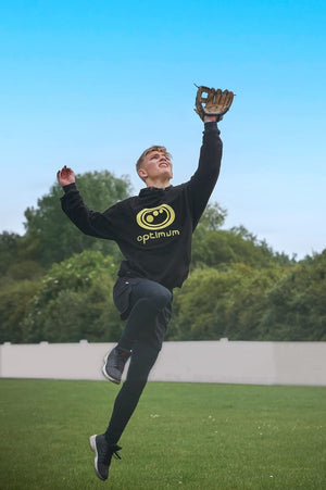 Player in black Optimum hoodie leaping to catch with tan baseball glove under blue sky - Optimum