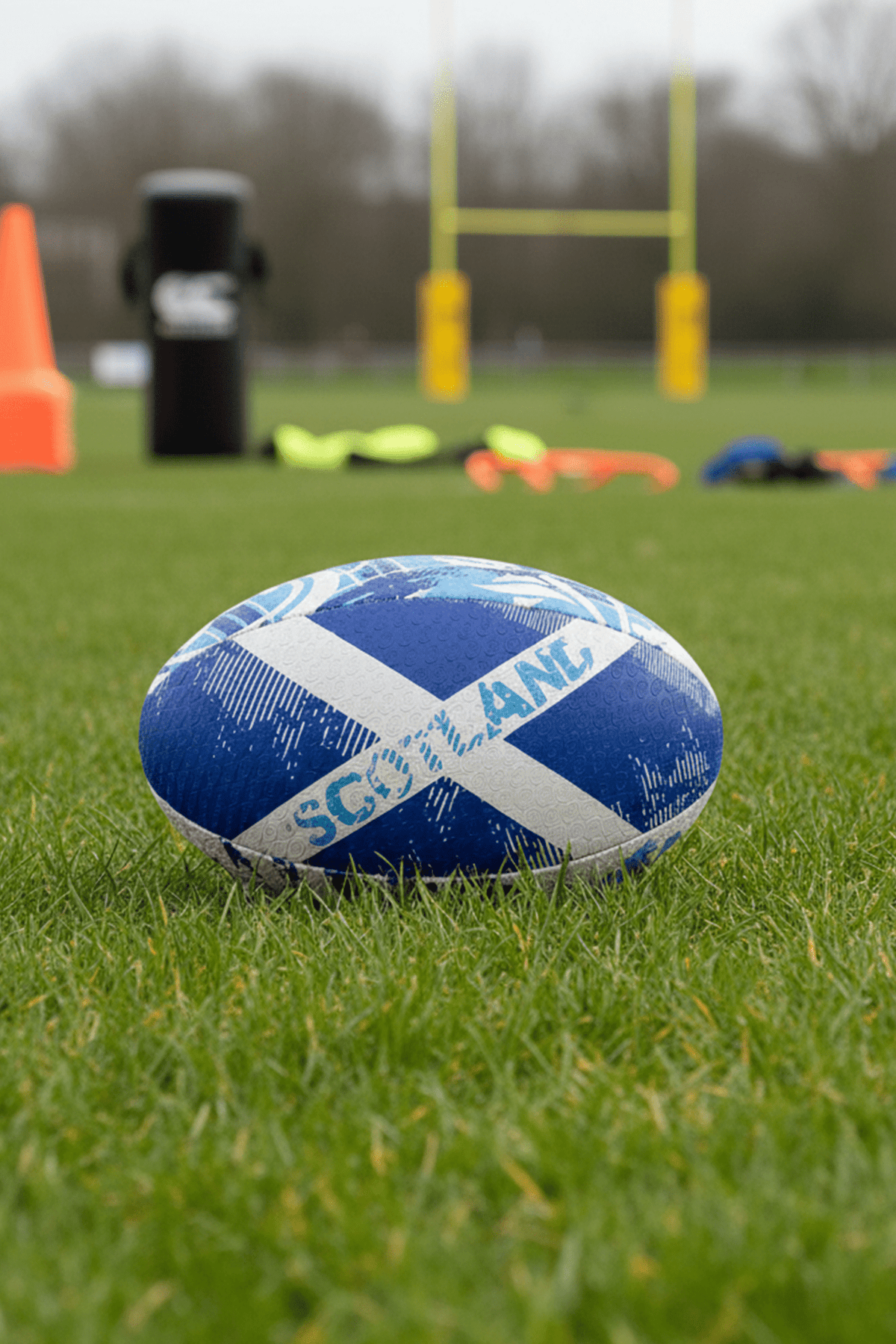 Blue Optimum Scotland rugby ball with white saltire and SCOTLAND print on grass by rugby posts - Optimum